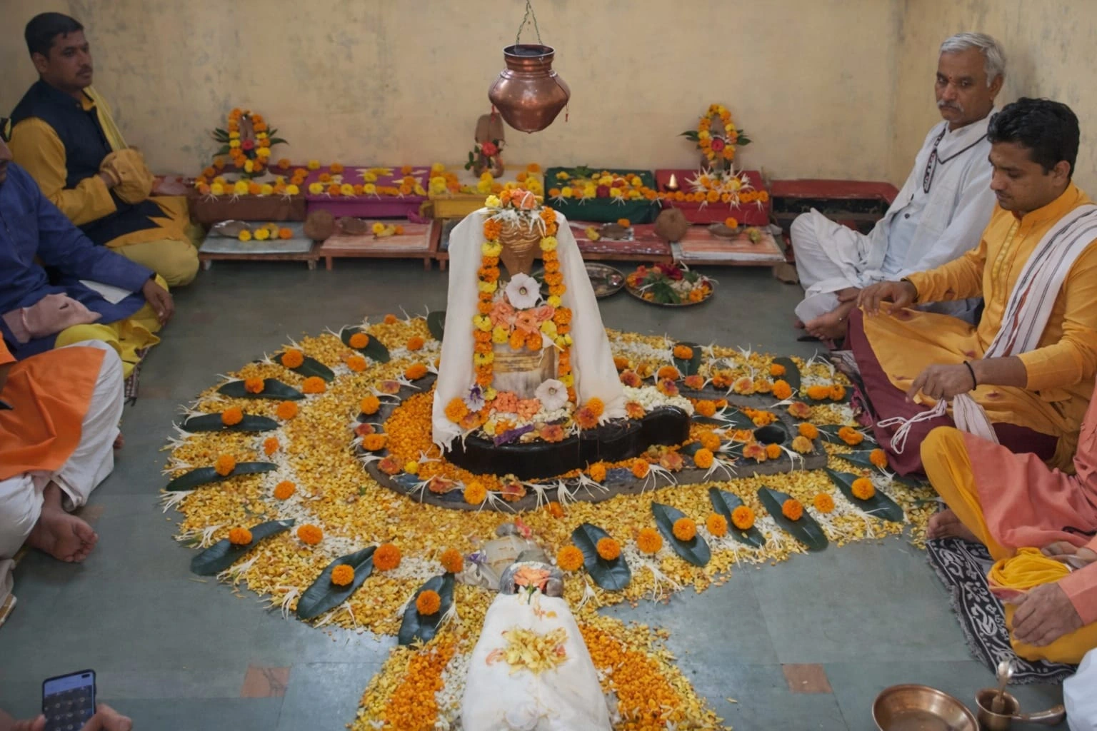 Mahamrityunjaya Jaap ritual at Trimbakeshwar Shivling decorated with marigold flowers, Abhishek Kalash above, and pandits seated around performing Jaap
