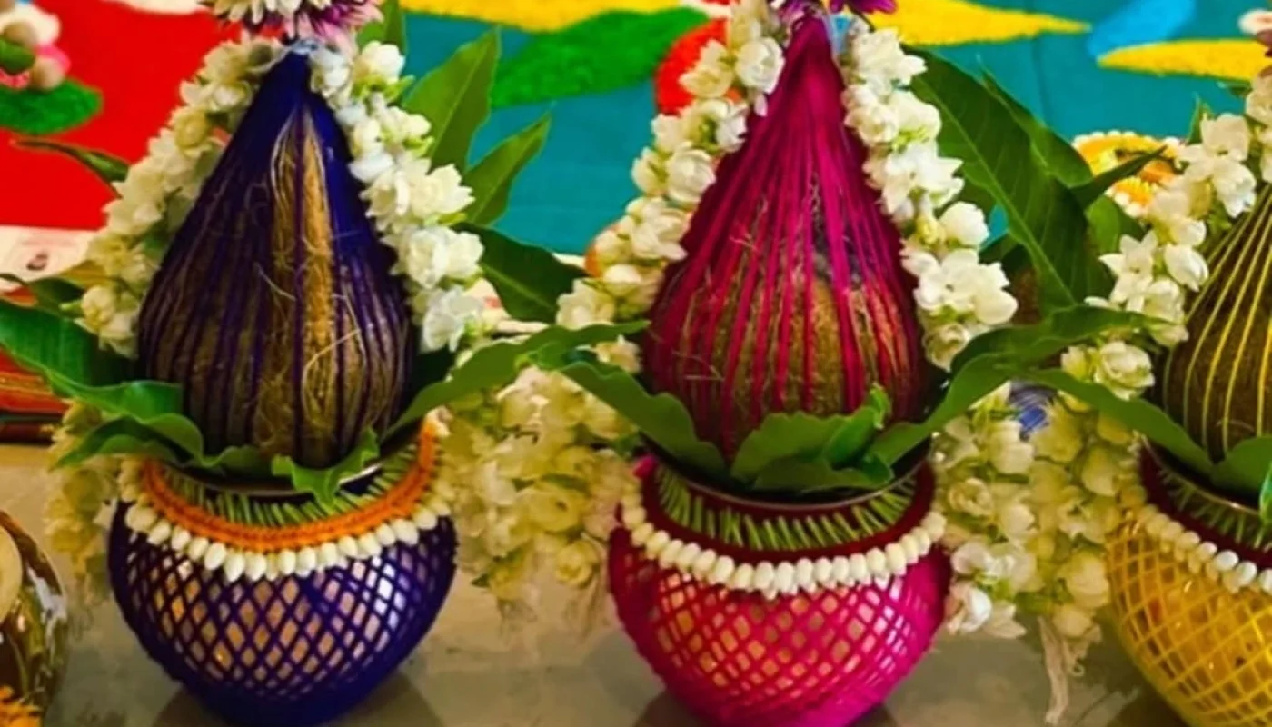 Three decorated kalash in blue, pink, and yellow with jasmine garlands and mango leaves for home puja setup