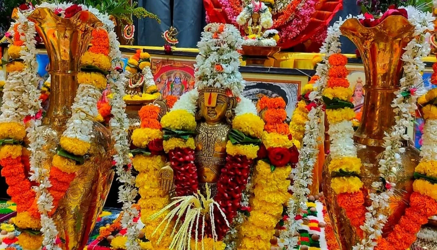 Grand Vishnu Puja with a beautifully decorated deity idol, fresh flower garlands, and traditional brass ritual vessels—a large-scale temple and community puja service.