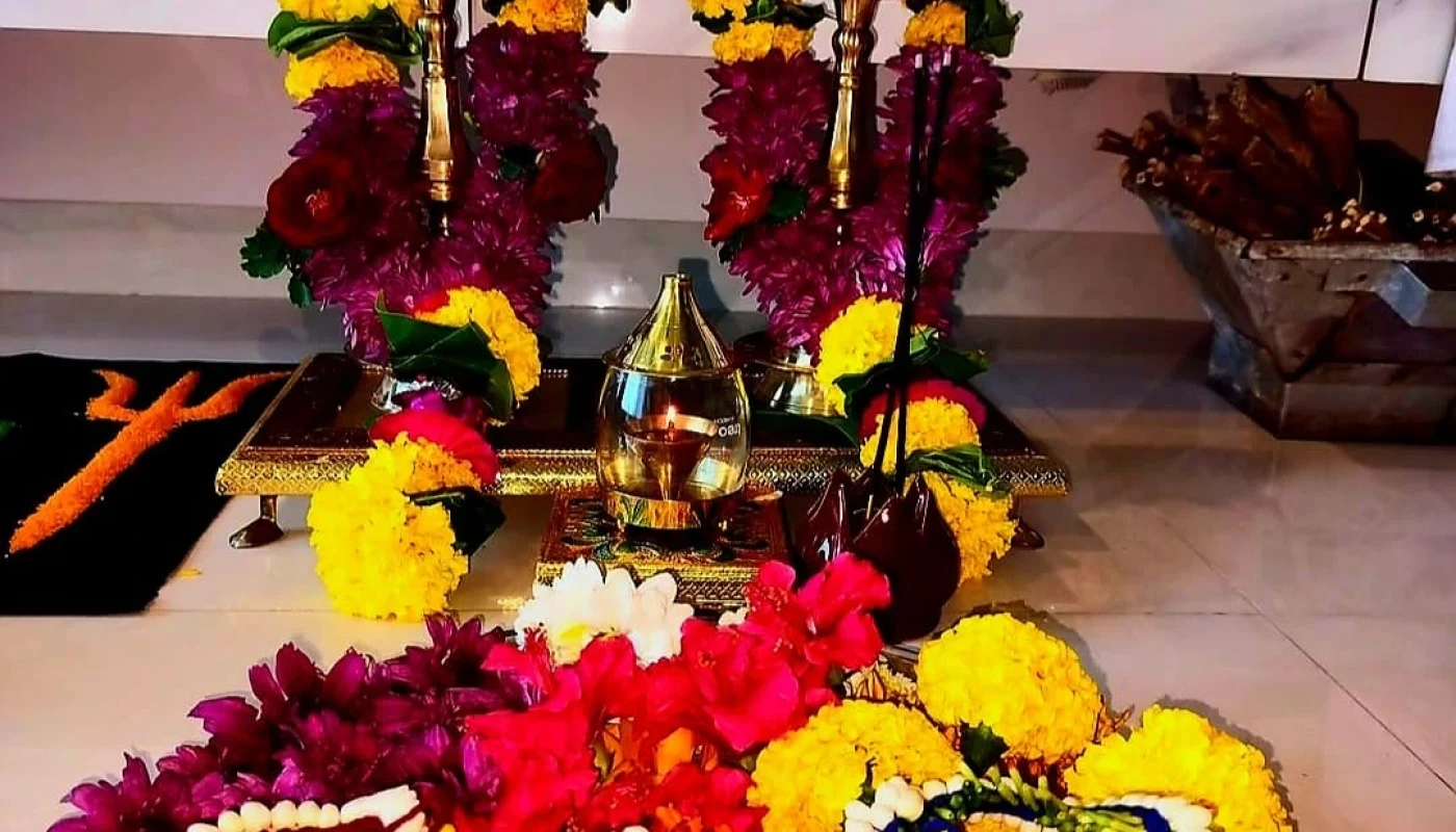 Two brass deepam lamp stands decorated with yellow and purple flower garlands, along with an Om symbol flower thali, a beautiful traditional home puja decoration.