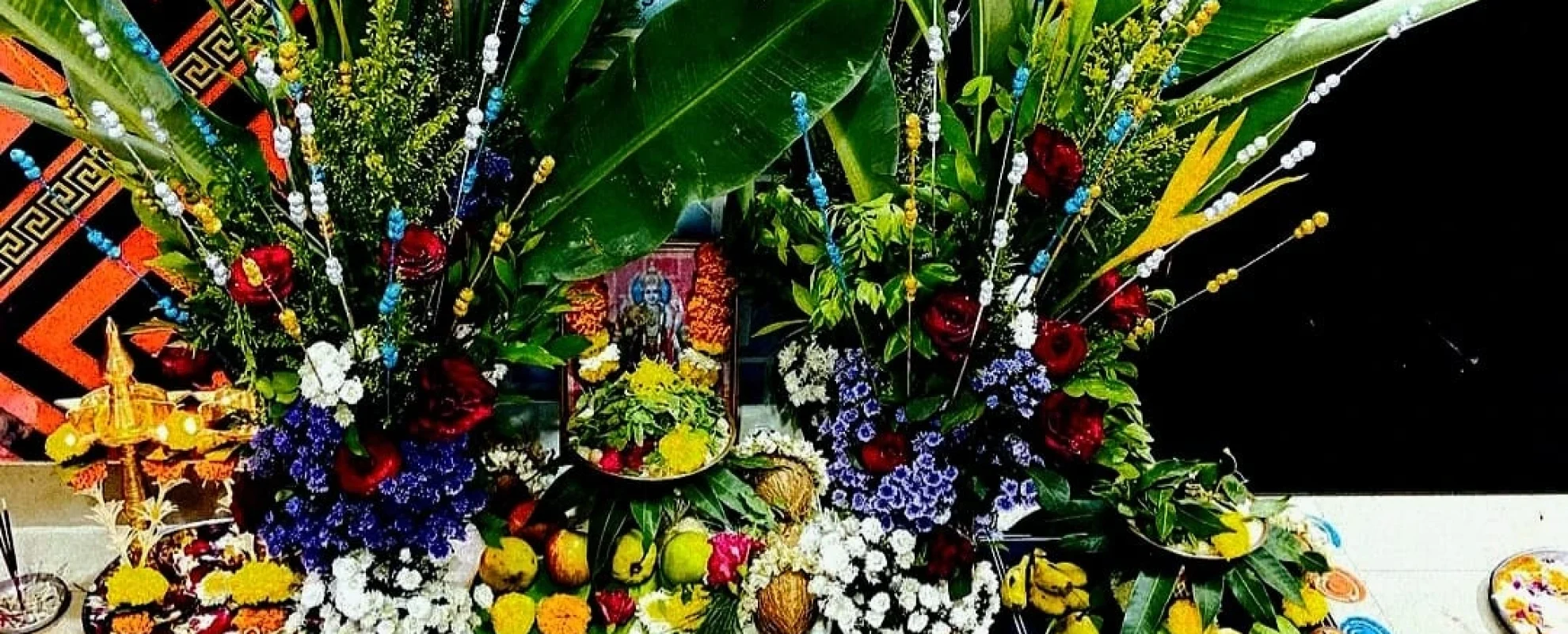 Elaborate home puja decoration with banana leaves, fresh mixed flowers, and a deity photo. Navchandi Puja was performed at home by Pandit Ramachandra Guruji.